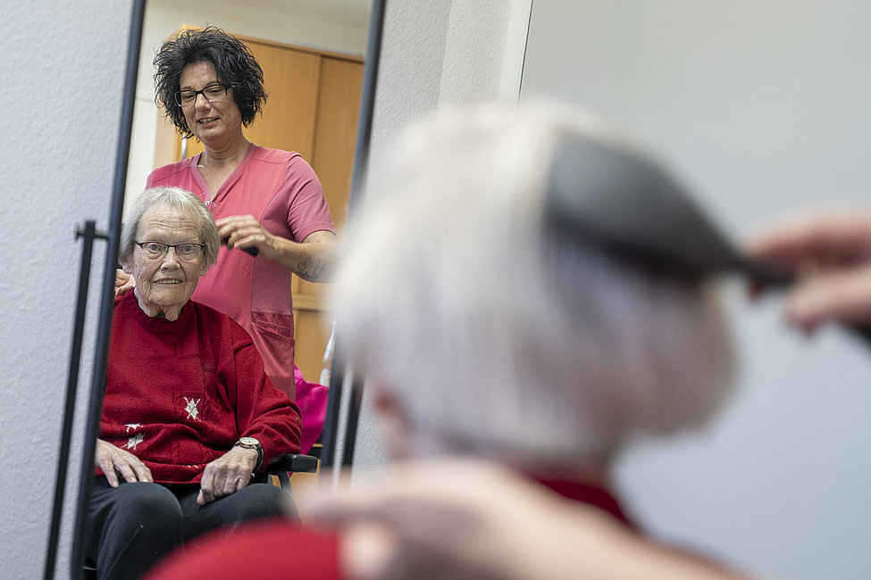Pflegekraft bürstet der älteren Frau im Rollstuhl die Haare